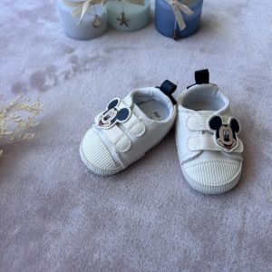 Petites chaussures blanches pour bébé, ornées d’un motif Mickey sur la languette, avec fermeture à scratchs, posées sur un tissu doux, d'occasion