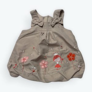 Robe bébé beige sans manches avec broderies florales et petit personnage, ornée de nœuds aux épaules. Seconde main.